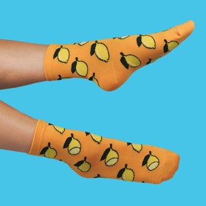 Könnte beinhalten: Ein Paar orangefarbene Socken mit einem Zitronenmuster. Die Socken befinden sich an den Füßen einer Person.