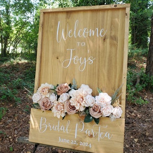 May include: Wooden sign with a floral arrangement and the text "Welcome to Joy's Bridal ParTea June 22, 2024".