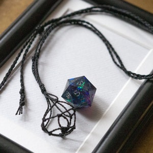 Könnte beinhalten: Eine schwarze Schnurkette mit einem schwarzen Makramee-Knoten am Ende, an dem ein regenbogenfarbener blauer, grüner und violetter Harz-W20-Würfel hängt.