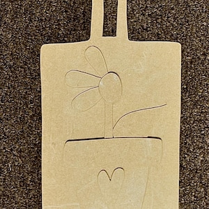 May include: A light brown wooden cutting board with a handle. The board features a flower in a pot design with a heart shape. The flower has five petals and a stem. The pot has a heart shape cut out.