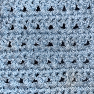 May include: A close-up of a light blue crocheted fabric with a repeating pattern of small holes.
