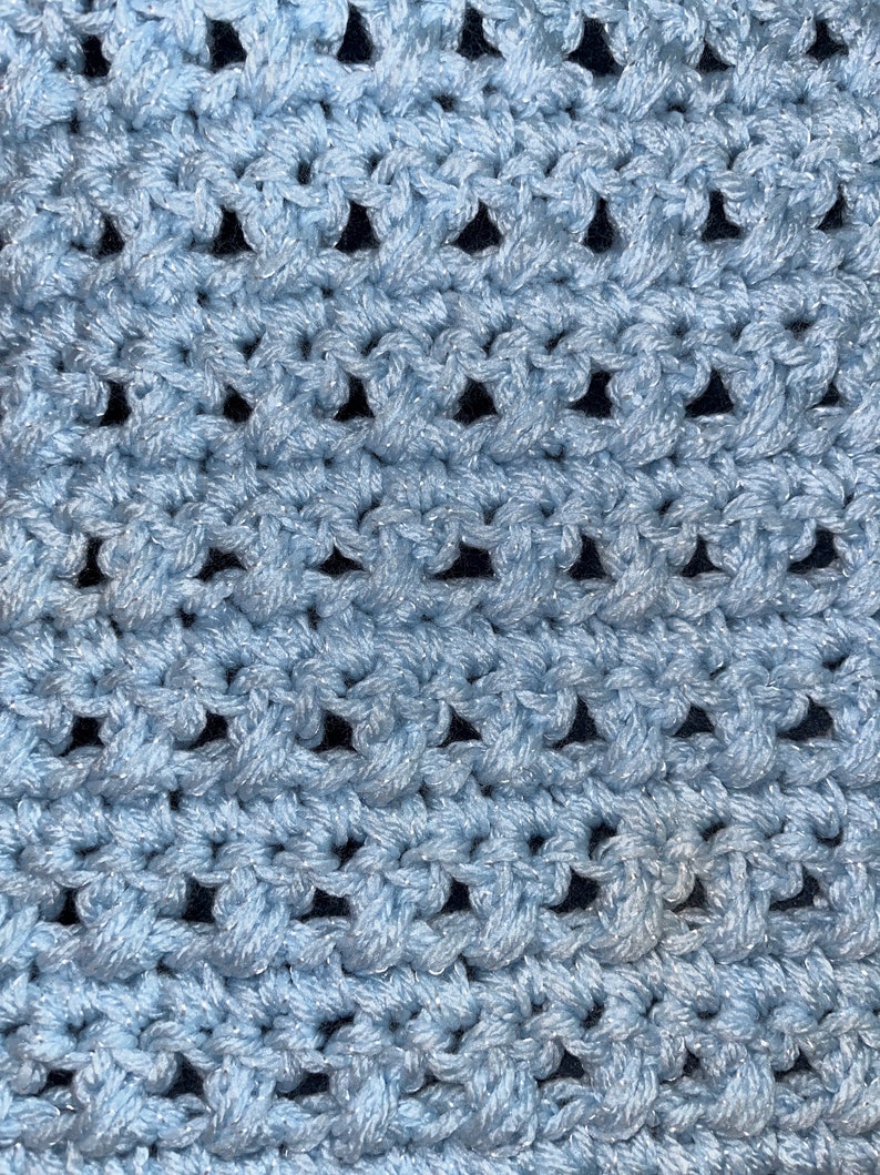 May include: A close-up of a light blue crocheted fabric with a repeating pattern of small holes.