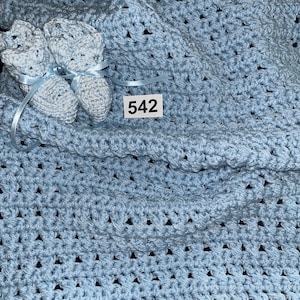 May include: A light blue crocheted baby blanket with matching booties. The blanket has a simple, repeating pattern. The booties have a white and blue color scheme. The tag on the blanket reads "542".