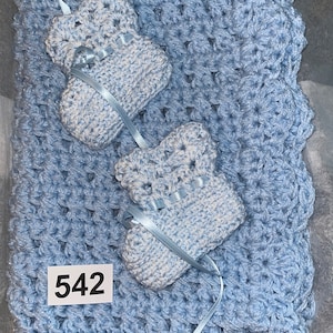 May include: A light blue crocheted baby blanket with two matching booties. The blanket has a scalloped edge and the booties have a white and blue pattern. The number 542 is written on a white tag attached to the blanket.