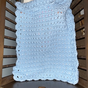 May include: A light blue crocheted baby blanket with a scalloped edge, folded in a crib.