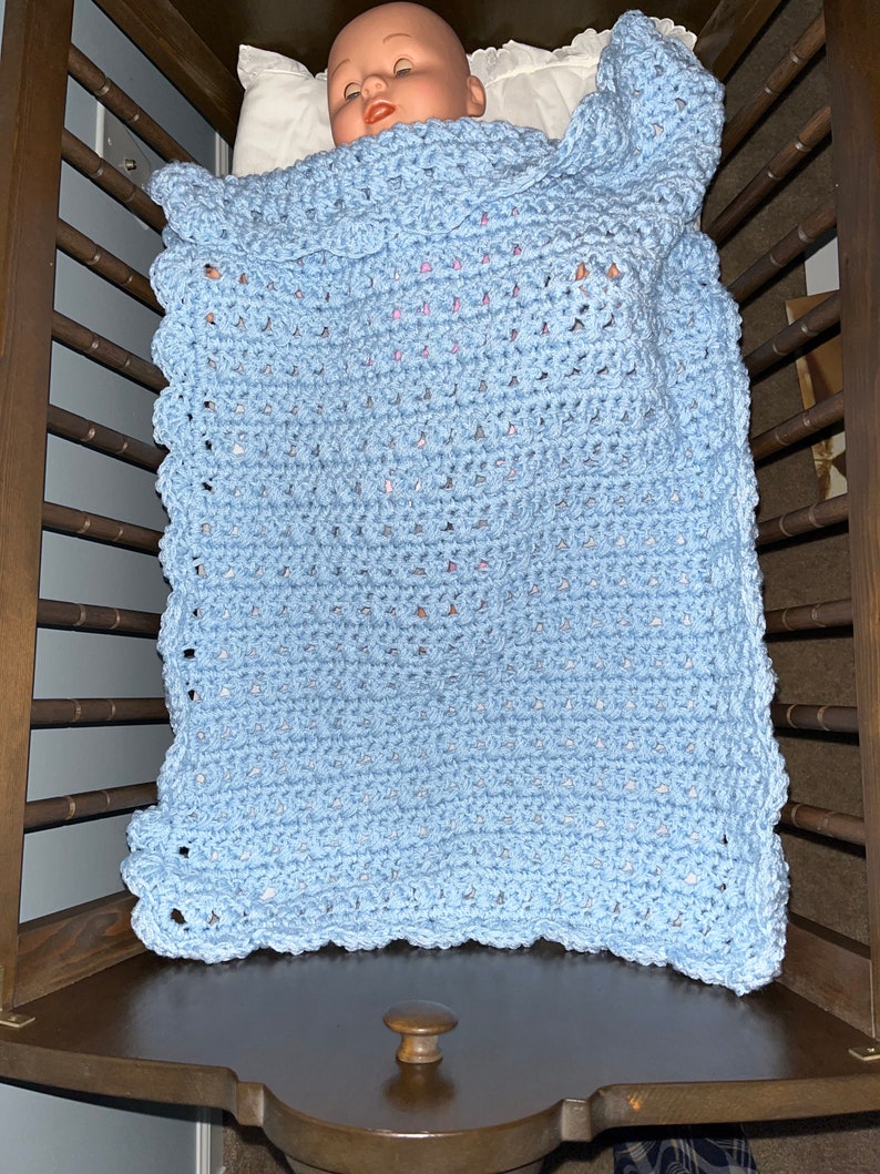 May include: A light blue crocheted baby blanket with a scalloped edge, folded in a crib.