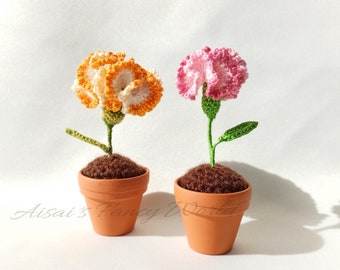 以下が含まれることがあります： 鉢植えのクロシェのカーネーションの花が2つ。左の花はオレンジと白、右の花はピンクと白です。