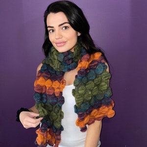 May include: A multi-colored chunky knit scarf with a textured, bubble-like design. The scarf is made in shades of green, blue, orange, and brown.