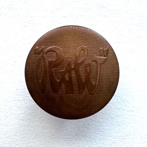 May include: A round, brown, metal button with the word "Rabbit" embossed on it.