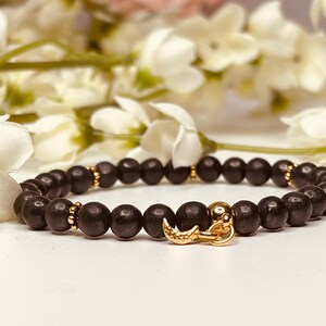 Könnte beinhalten: Ein schwarzes Perlenarmband mit einem goldenen Halbmond-Anhänger. Das Armband besteht aus kleinen, runden Perlen und hat ein schlichtes, elegantes Design.