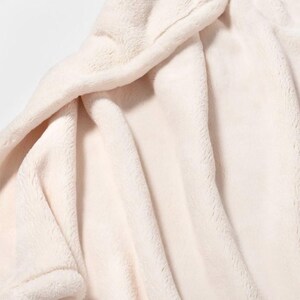 May include: A soft, white plush blanket with a smooth, fuzzy texture. The blanket is folded and draped over a surface, showcasing its luxurious feel.