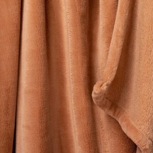 May include: A close-up of a soft, peach-colored throw blanket with a fuzzy texture.
