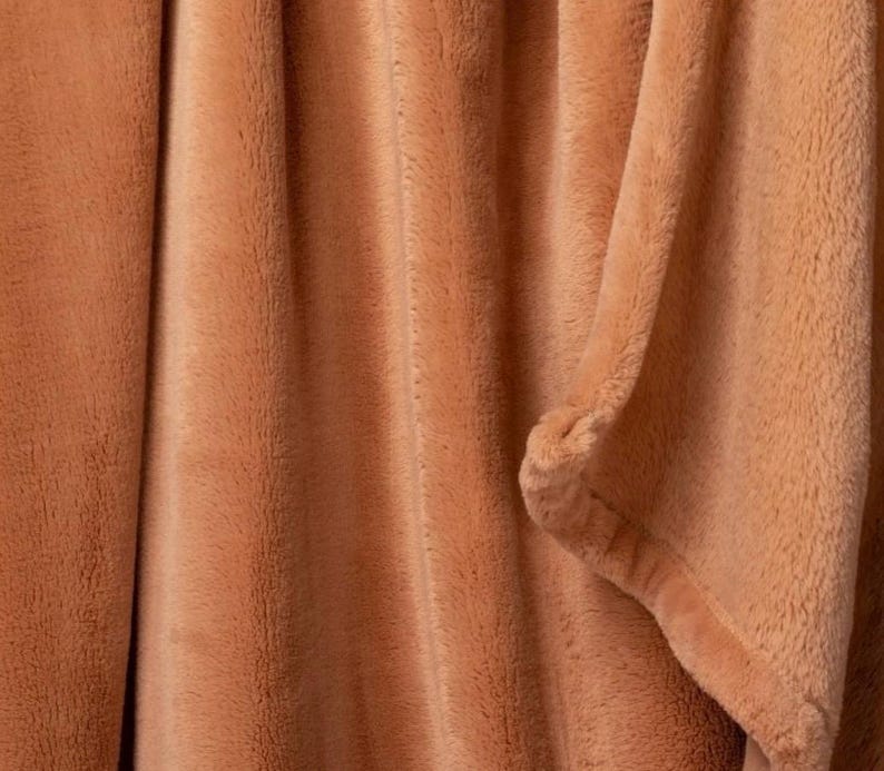 May include: A close-up of a soft, peach-colored throw blanket with a fuzzy texture.
