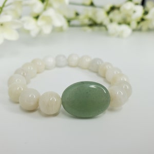 May include: A white and green beaded bracelet with a large oval green stone charm. The bracelet is made of round beads and is strung on a stretchy cord.