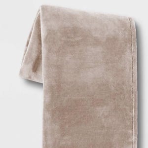 May include: A soft, plush throw blanket in a light beige color. The blanket is folded and draped over a white surface.
