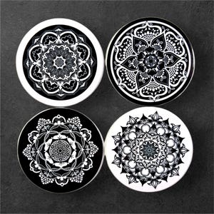 Puede incluir: Cuatro posavasos negros y blancos con intrincados diseños de mandalas. Cada posavasos presenta un patrón de mandala diferente con un diseño blanco sobre un fondo negro.
