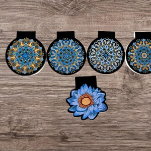 Può includere: Cinque segnalibri rotondi con motivi neri e blu con un segnalibro a forma di fiore blu al centro.