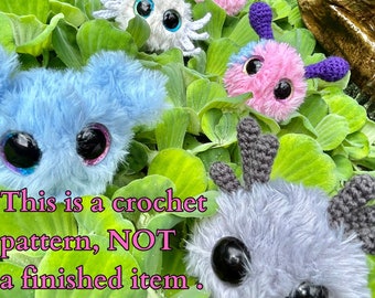 May include: A crochet pattern for a plush toy. The pattern includes five different plush toys in various colors, including white, blue, pink, and gray. The toys have large eyes and are shown in a green leafy setting. This is a crochet pattern, NOT a finished item.