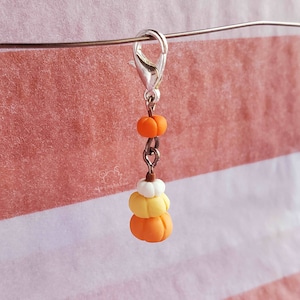 May include: A silver charm with a stack of three miniature pumpkins. The pumpkins are orange, yellow, and white. The charm is attached to a silver chain.