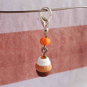 May include: A silver charm with a small orange pumpkin and a miniature pumpkin spice cupcake with white frosting and a small orange pumpkin on top.