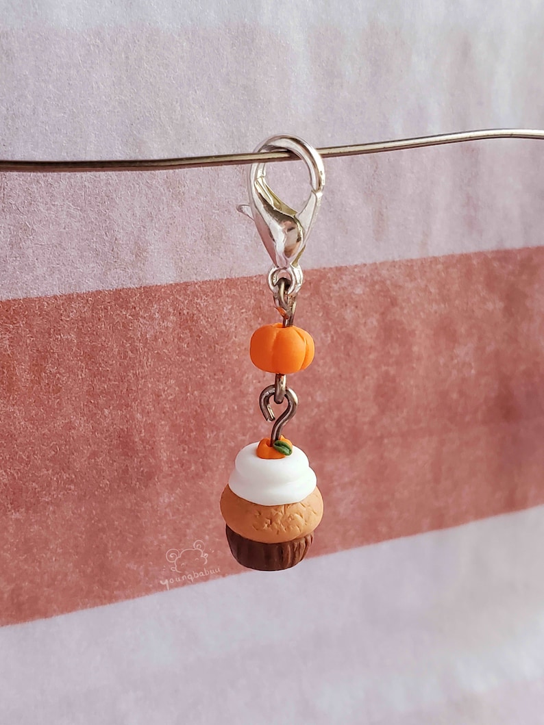May include: A silver charm with a small orange pumpkin and a miniature pumpkin spice cupcake with white frosting and a small orange pumpkin on top.