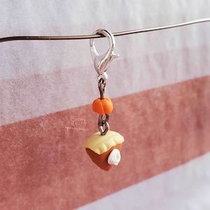 May include: A silver charm with a small orange pumpkin and a slice of pie with a white dollop of whipped cream. The charm is attached to a silver chain and a silver lobster clasp.