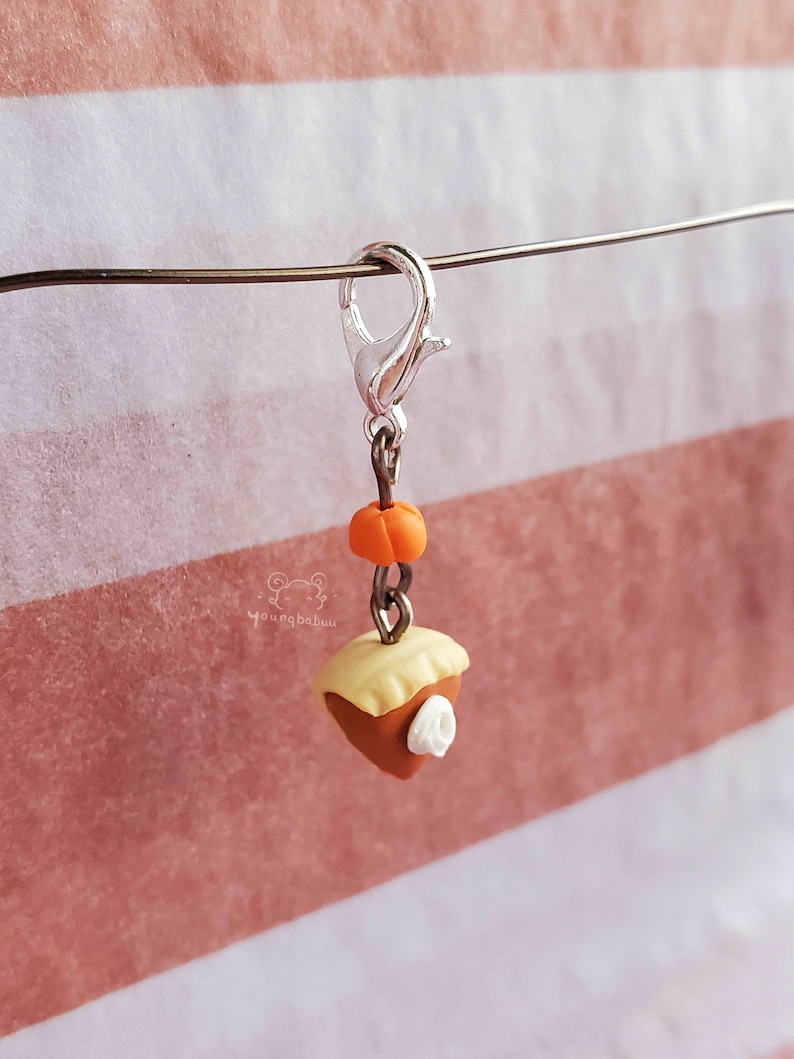 May include: A silver charm with a small orange pumpkin and a slice of pie with a white dollop of whipped cream. The charm is attached to a silver chain and a silver lobster clasp.