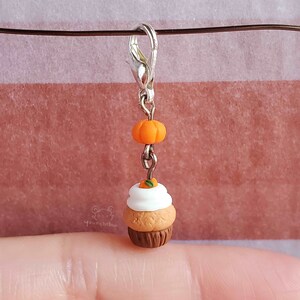 May include: A small, brown and white cupcake charm with a miniature orange pumpkin on top. The charm is attached to a silver lobster clasp.
