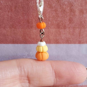 May include: A silver charm with a stack of three miniature pumpkins. The pumpkins are orange, yellow, and white. The charm is attached to a silver chain.