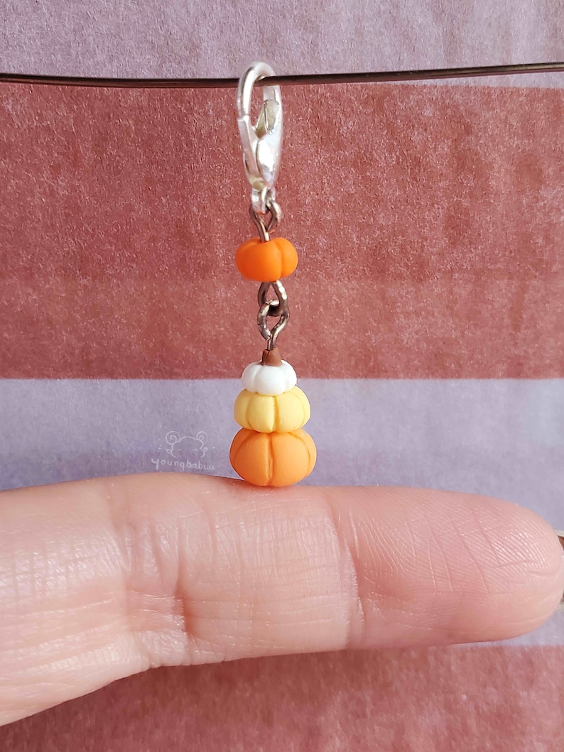 May include: A silver charm with a stack of three miniature pumpkins. The pumpkins are orange, yellow, and white. The charm is attached to a silver chain.