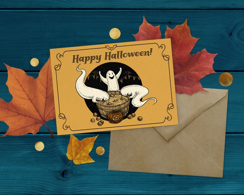 May include: A yellow card with the text "Happy Halloween!" and a drawing of three ghosts in a cauldron with a pumpkin. The card is on a brown envelope and a blue wooden background with fall leaves.