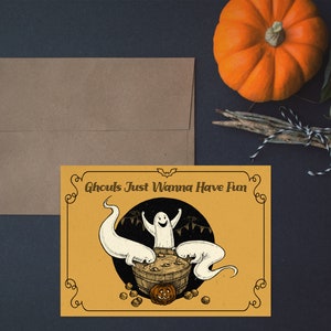 May include: A yellow card with a black border and a black and white illustration of three ghosts in a cauldron. The text on the card reads "Ghouls Just Wanna Have Fun".