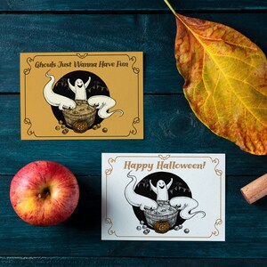 May include: Two Halloween greeting cards with a black and white illustration of ghosts in a cauldron. The top card has a yellow background and says "Ghouls Just Wanna Have Fun". The bottom card has a white background and says "Happy Halloween!"