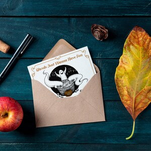 May include: A brown envelope with a white card inside. The card has a black and white illustration of a ghost in a cauldron with other ghosts around it. The text on the card reads "Ghouls Just Wanna Have Fun".