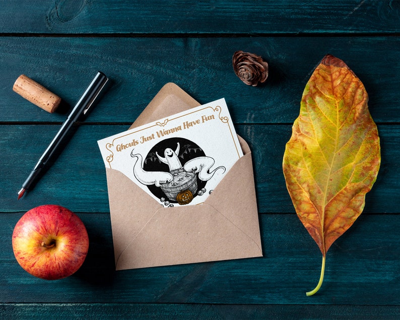 May include: A brown envelope with a white card inside. The card has a black and white illustration of a ghost in a cauldron with other ghosts around it. The text on the card reads "Ghouls Just Wanna Have Fun".