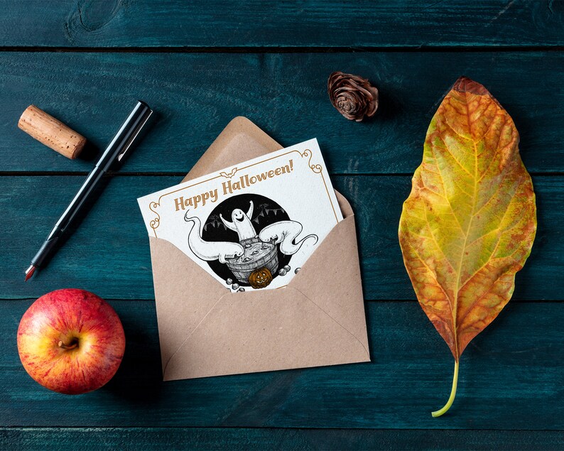 May include: A brown envelope with a white card inside. The card has a black and white illustration of a ghost in a cauldron with the text "Happy Halloween!" in gold lettering.