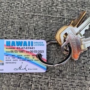 K&ouml;nnte beinhalten: Ein hawaiianischer F&uuml;hrerschein mit dem Namen McLovin und einem Foto, befestigt an einem Schl&uuml;sselring mit mehreren Schl&uuml;sseln. Der F&uuml;hrerschein enth&auml;lt Details wie Geburtsdatum, Gr&ouml;&szlig;e und Ablaufdatum.