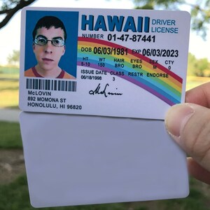 K&ouml;nnte beinhalten: Ein hawaiianischer F&uuml;hrerschein mit dem Namen McLovin, Geburtsdatum 03.06.1981 und Ablaufdatum 03.06.2023. Der F&uuml;hrerschein zeigt ein Foto einer Person mit Brille und einem orange-roten Hemd. Der F&uuml;hrerschein enth&auml;lt auch ein Regenbogen-Design.