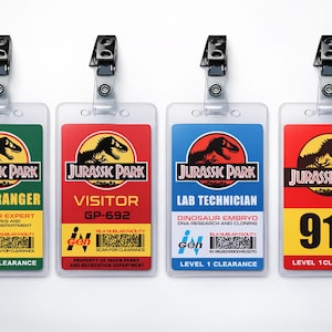Puede incluir: Cuatro insignias de identificaci&oacute;n de Jurassic Park de pl&aacute;stico con clips negros. Las insignias presentan el logotipo de Jurassic Park y texto que identifica roles: Park Ranger, Visitor, Lab Technician y 916. Cada insignia tiene un esquema de color y texto &uacute;nicos.