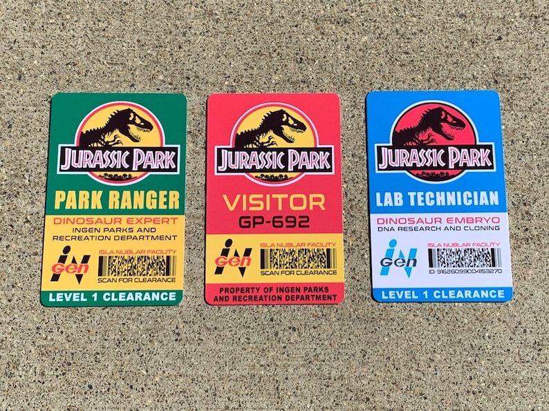 Puede incluir: Tres tarjetas de identificaci&oacute;n de Jurassic Park: verde para Guardabosques, roja para Visitante y azul para T&eacute;cnico de laboratorio. Cada una presenta el logotipo de Jurassic Park y detalles de los roles.