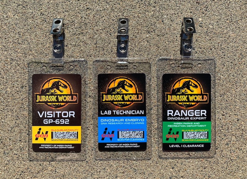 Puede incluir: Tres identificaciones de pl&aacute;stico transparente con clips met&aacute;licos. Cada identificaci&oacute;n presenta el logotipo de "Jurassic World" y diferentes t&iacute;tulos: "Visitante", "T&eacute;cnico de laboratorio" y "Ranger". Las identificaciones incluyen texto como "GP-692", "Embri&oacute;n de dinosaurio" y "Nivel 1 de autorizaci&oacute;n".