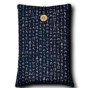 May include: A navy blue book sleeve with a white Japanese script pattern. The sleeve is secured with a black cord and a wooden button closure. The book cover is rectangular and has a soft appearance.