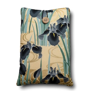 May include: A rectangular fabric pouch featuring a floral pattern of dark blue irises and green leaves on a light beige background with gold swirling lines. The pouch is secured at the top with a black elastic cord and a round wooden button.