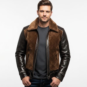 Puede incluir: Chaqueta de borrego marrón con mangas y detalles en cuero marrón oscuro. La chaqueta tiene un cuello de borrego y cierre de cremallera frontal. El modelo lleva una camiseta gris y vaqueros azules.