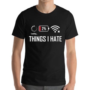 Puede incluir: Camiseta negra con el texto blanco "THINGS I HATE". Encima del texto hay tres gráficos blancos: un símbolo de carga, una batería al 2% y un símbolo wifi con una X.