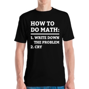 May include: Black t-shirt with white text: "HOW TO DO MATH: 1. WRITE DOWN THE PROBLEM 2. CRY". The shirt has a crew neck and is likely made of a soft fabric. The text is in a clear, bold font.