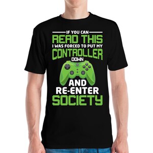May include: Black t-shirt with a green video game controller graphic. The shirt has the text "IF YOU CAN READ THIS I WAS FORCED TO PUT MY CONTROLLER DOWN AND RE-ENTER SOCIETY" in white and green.