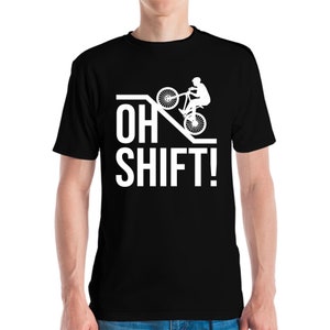 Könnte beinhalten: Schwarzes T-Shirt mit einem weißen Aufdruck eines Radfahrers, der einen Wheelie auf einer Rampe macht, mit dem Text "OH SHIFT!" in Weiß. Das T-Shirt ist aus einem weichen Material.