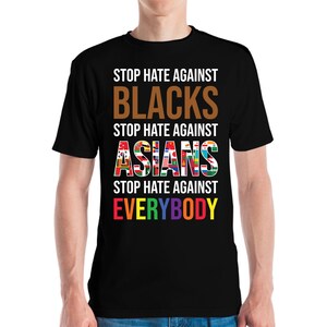 May include: Black t-shirt with the message "STOP HATE AGAINST BLACKS, ASIANS, EVERYBODY" in white, brown, and rainbow colors. The word "ASIANS" is filled with flags. A statement against hate.