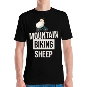 Könnte beinhalten: Schwarzes T-Shirt mit einem Cartoon-Schaf, das Fahrrad fährt. Der Text "MOUNTAIN BIKING SHEEP" ist in Weiß gedruckt, mit "BIKING" in einem weißen Feld. Das Schaf ist weiß mit einem braunen Gesicht und trägt einen Helm.